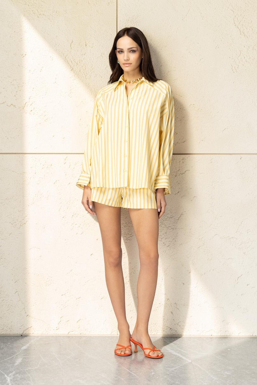 Model trägt ein gelb-weiß gestreiftes artekozio Set aus langärmeligem Hemd und Shorts für einen sommerlichen Look.